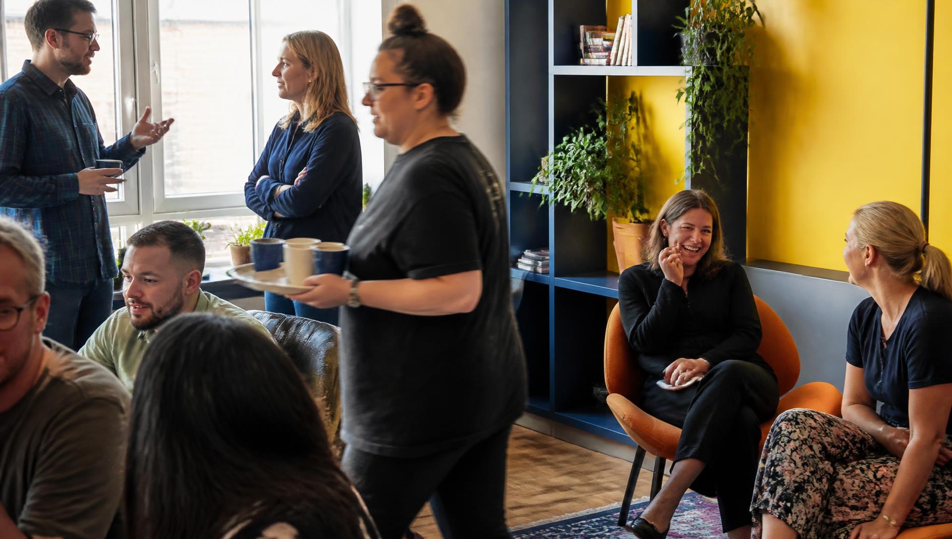 People sharing food around a long table in a community kitchen, mid-conversation